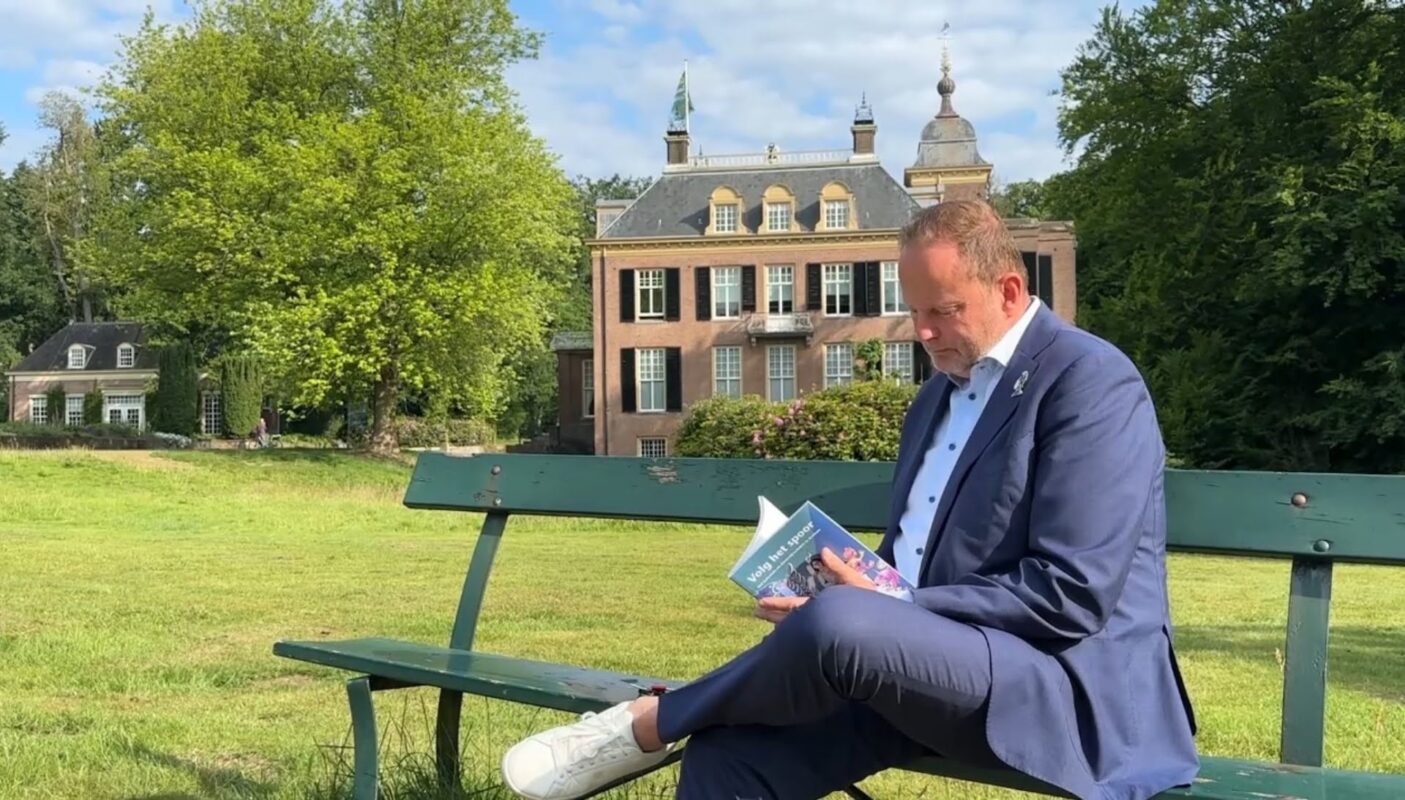 Wethouder inclusie Maurits van de Geijn zit op een bankje bij Huis Zypendaal en bladert door het boek 'Volg het spoor'